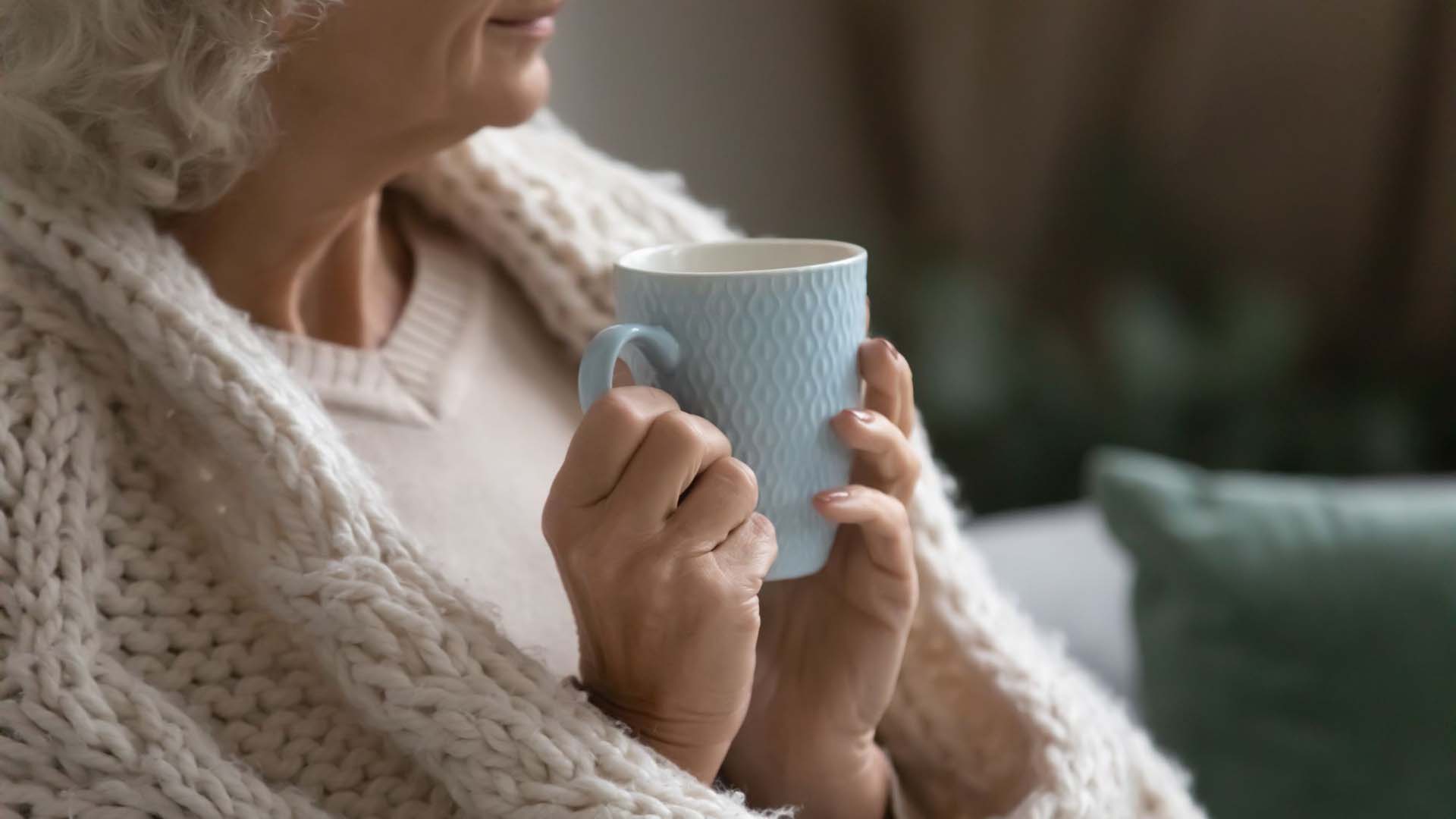 Senior lady holding a mug while wrapped up in a thick blanket