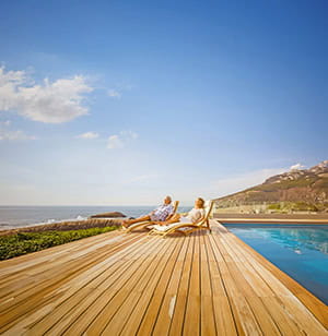  Older couple enjoying a sunny day relaxing on sunloungers by a swimming pool. 