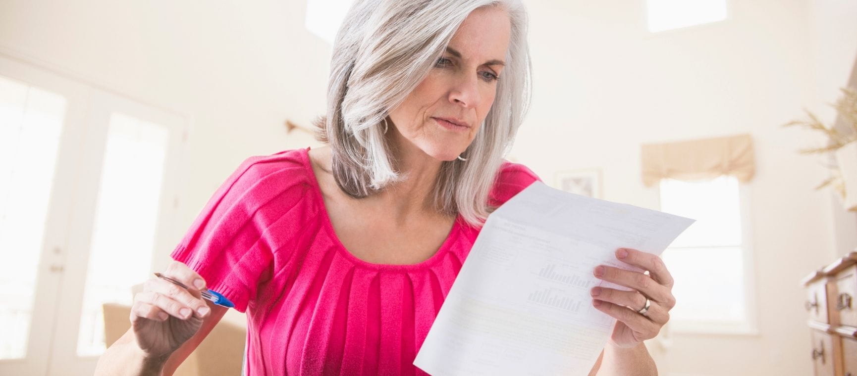A woman in a pink top checking a bill in her home