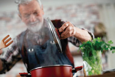 Mature man in a kitchen, holding the lid of a pot with steam billowing up in front