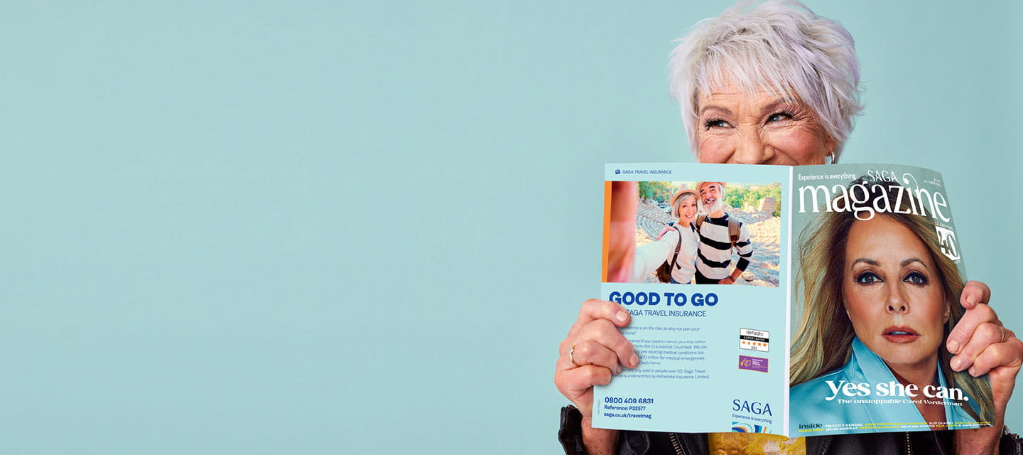 Older person reading Saga Magazine and peering at the viewer over the edge